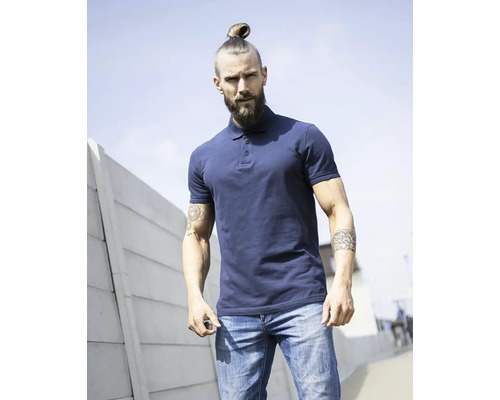 Muž s bradou a drdolom nosí polokošeľu a džínsy