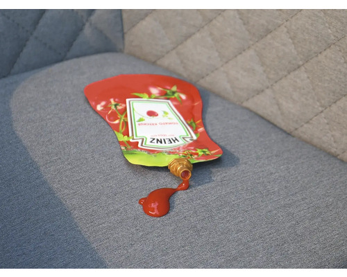 Rozliata fľaša kečupu na čalúnenom nábytku