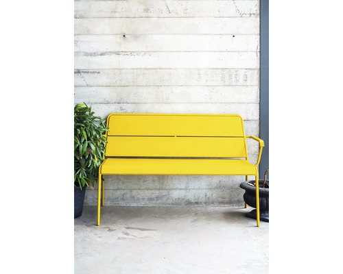 Žltá kovová lavica vonku pred betónovou stenou