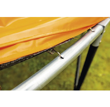 Detailný pohľad na pružinu trampolíny, ktorá pripevňuje oranžový ochranný kryt k rámu trampolíny.