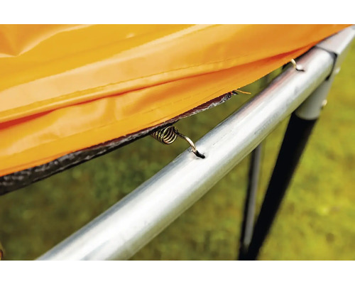 Detailný pohľad na pružinu trampolíny, ktorá pripevňuje oranžový ochranný kryt k rámu trampolíny.