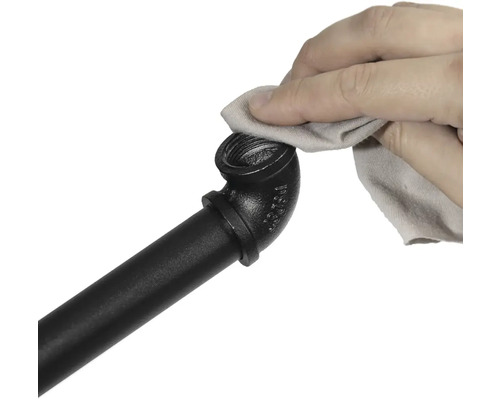 Ruka čistí čiernu rúrkovú armatúru handričkou.