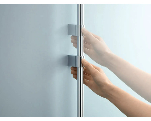 Osoba nastavuje sprchovú tyč s nástenným držiakom.