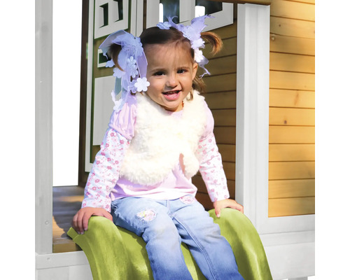 Dievča sedí na šmýkačke pred dreveným domčekom na hranie.