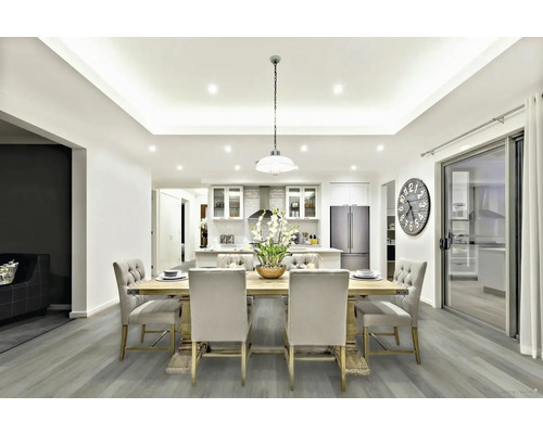 Svetlý obývací priestor s jedálenským stolom, stoličkami, osvetlením a kuchynským kútom.