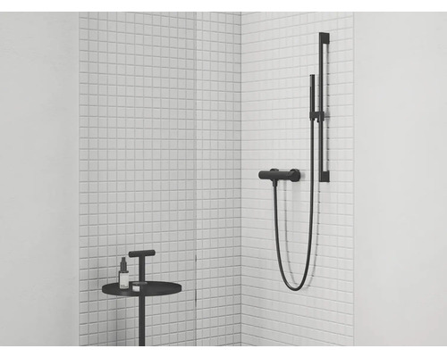 Roh kúpeľne s bielymi obkladmi, čiernou sprchovou batériou a malým stolom