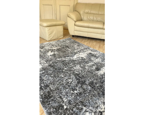 Koberec s abstraktným vzorom, umiestnený v obývacej izbe s pohovkou a stoličkou