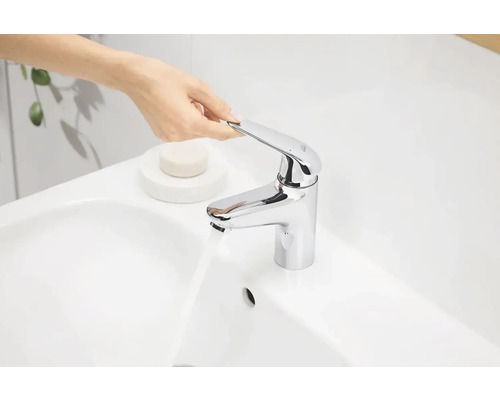 Osoba ovláda chrómovanú vodovodnú batériu na bielom umývadle