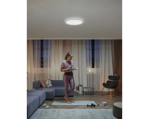 Žena stojí na podložke na jogu v obývacej izbe s okrúhlym stropným svietidlom.