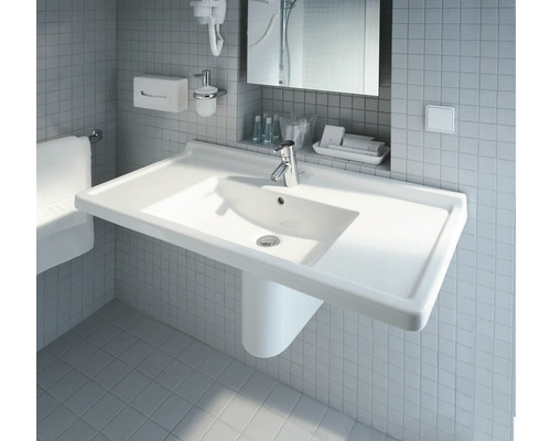 Biele umývadlo s vodovodnou batériou v kúpeľni pred obkladanou stenou.