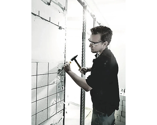 Muž odstraňuje dlaždice zo steny pomocou kladiva a dláta.