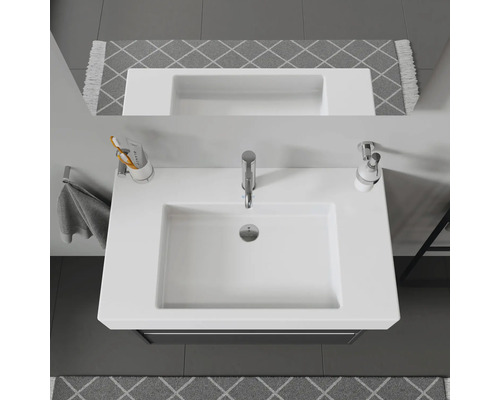 Pohľad zhora na biele umývadlo s batériou, dávkovačom mydla a držiakom na zubné kefky v kúpeľni