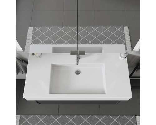 Pohľad zhora na umývadlo s vodovodnou batériou, dávkovačom mydla a vzorovanými kobercami v kúpeľni.