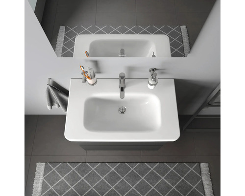 Pohľad zhora na umývadlo v kúpeľni s vodovodnou batériou, dávkovačom mydla, pohárom na zubné kefky a uterákom