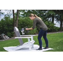 Žena strieka farbu na záhradnú stoličku Adirondack pomocou striekacej pištole.