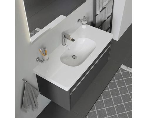 Moderná kúpeľňa s umývadlom, skrinkou, batériou, dávkovačom mydla, uterákom a ďalším kúpeľňovým príslušenstvom.