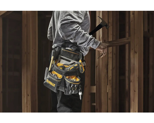 Remeselník s taškou na náradie a náradím pri drevenom ráme.