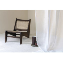 Scéna s tmavou drevenou stoličkou s ratanovým sedadlom, džbánom a šálkou na podnose a priehľadným závesom.