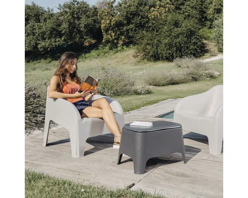 Vonkajšia scéna so ženou čítajúcou knihu v sivom záhradnom kresle a sivým záhradným stolíkom vedľa