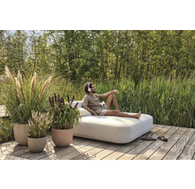 Scéna s osobou na záhradnom ležadle obklopenom rastlinami v kvetináčoch.