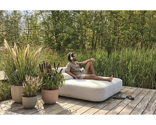 Scéna s osobou na záhradnom ležadle obklopenom rastlinami v kvetináčoch.