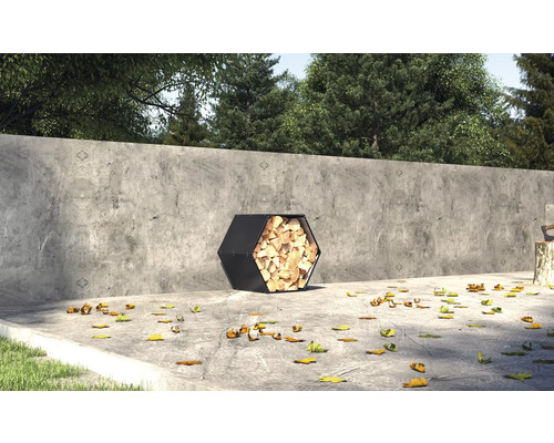 Šesťhranný kovový kôš na drevo plný dreva vonku pred betónovým múrom