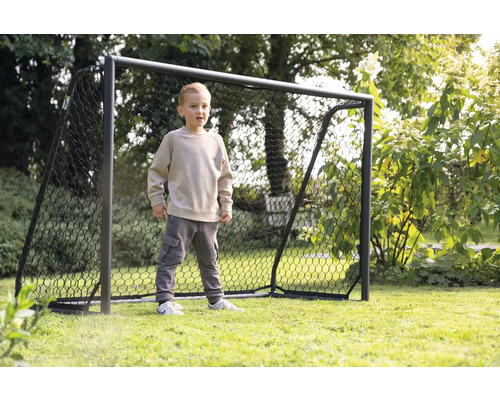 Chlapec stojí pred futbalovou bránkou v záhrade.