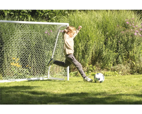 Chlapec kope do futbalovej lopty pred futbalovou bránkou v záhrade