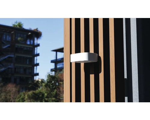 Biele vonkajšie svietidlo je pripevnené k drevenej fasáde.