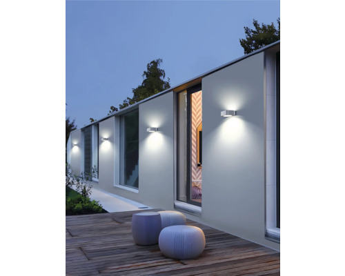 Osvetlená stena domu s vonkajšími svetlami a sedením na drevenej terase.