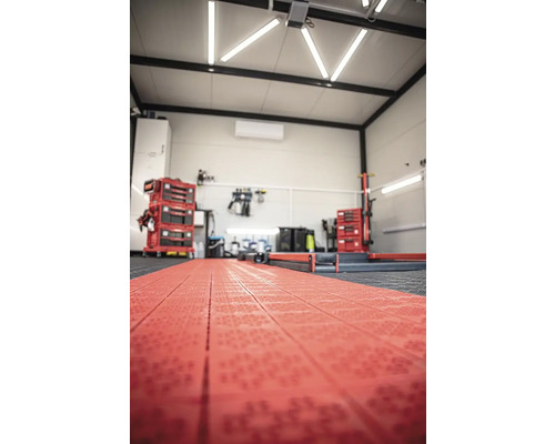 Dielňa s červenou podlahovou krytinou, vozíkom na náradie a pracovným stolom