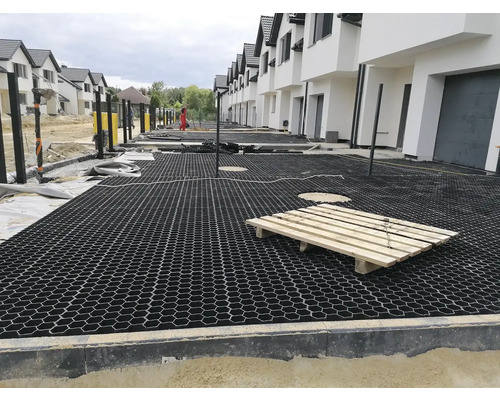 Pohľad na stavenisko s položenými zatrávňovacími dlaždicami pred radom domov.