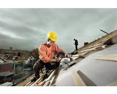 Muž s ochrannou prilbou pracuje s ručnou okružnou pílou na streche.