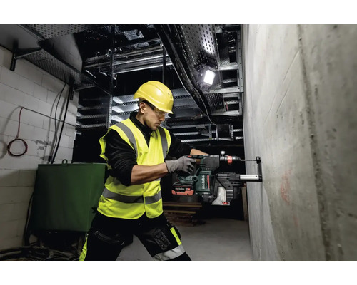 Muž vŕta s vŕtacím kladivom otvor do betónovej steny na stavenisku.