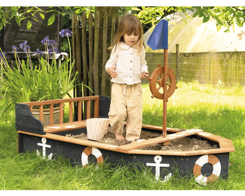 Dieťa sa hrá v pieskovisku v tvare lode s volantom a modrou plachtou