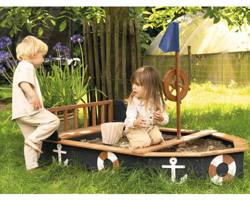 Dve deti sa hrajú v pieskovisku v tvare lode v záhrade.