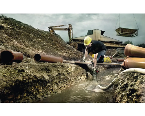 Stavenisko s robotníkom, bagrom a rúrami pri výkopových prácach