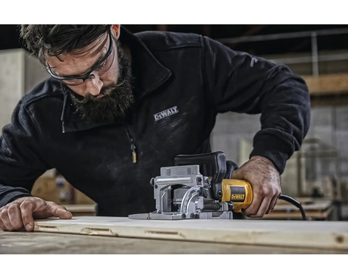 Muž používa lamelovaciu frézu DeWalt na drevenej doske. Logo DeWalt.