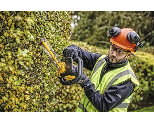 Osoba strihá živý plot nožnicami na živý plot a má na sebe ochranný odev.