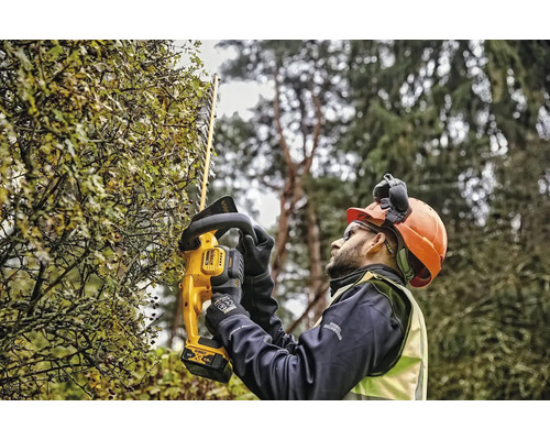Muž strihá živý plot pomocou akumulátorových nožníc na živý plot DeWalt
