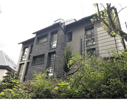 Viacpodlažný obytný dom s fasádou z kameňa a omietky a niekoľkými oknami.