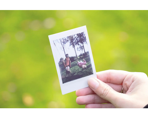 Ruka drží instantnú fotografiu s deťmi na hojdačkách