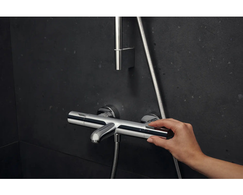 Nástenná sprchová batéria s ručným ovládaním na tmavom pozadí.