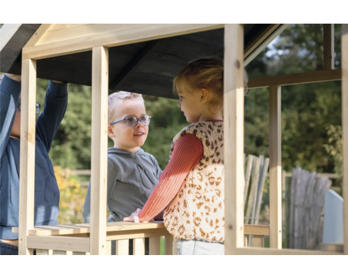 Dve deti sa hrajú v neošetrenom drevenom domčeku na hranie v záhrade.