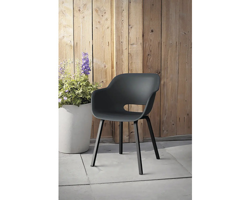 Plastová záhradná stolička s opierkami na ruky pred drevenou stenou