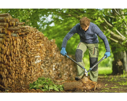 Muž štiepa drevo nožnicami na konáre vedľa hromady dreva.