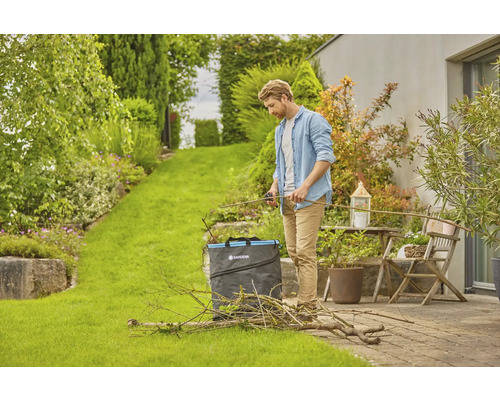 Muž strihá záhradný odpad záhradnými nožnicami a záhradným vrecom v záhrade.