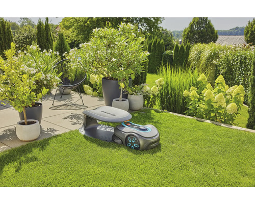 Scéna s robotickou kosačkou Gardena na trávniku, v pozadí rastliny a kríky.