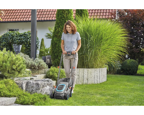 Žena používa kosačku na trávu v záhrade.