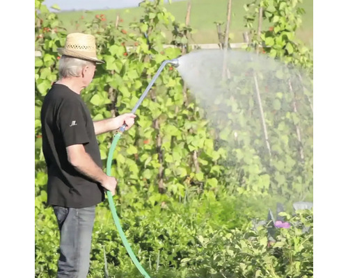Muž zavlažuje záhradu záhradnou hadicou a rozprašovacou tryskou.